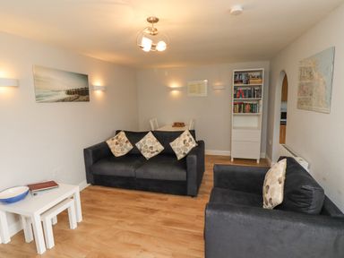 A living room with two black sofas with cushions a white bookshelf and a dining table at Bedwine Cottage in Beadnell