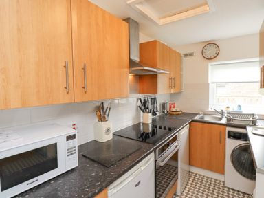 A kitchen with wooden cabinets a microwave stove oven sink and washing machine at Bedwine Cottage in Beadnell