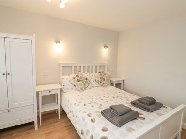 A bedroom with a double bed with heart patterned bedding two folded towels on bed two bedside tables and a white wardrobe at Bedwine Cottage in Beadnell