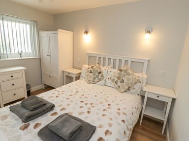 A bedroom with a double bed with patterned bedding two bedside tables a wardrobe and a chest of drawers at Bedwine Cottage in Beadnell