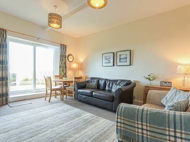 A living room with a black leather sofa a wooden dining table with chairs near sliding glass door and a beige armchair at Bellshill Cottage in Belford