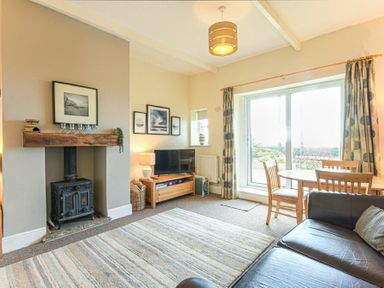 A living room with a wood stove and a dining table near sliding glass doors at Bellshill Cottage in Belford