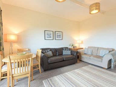 A living room with two sofas a wooden dining table with chairs and lamps at Bellshill Cottage in Belford