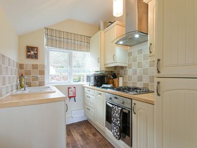 A small kitchen with wooden countertops a gas stove oven and a window with striped blinds at Bellshill Cottage in Belford