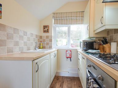 A kitchen with white cabinets and wooden countertops a window with striped blinds at Bellshill Cottage in Belford