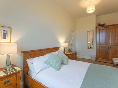 A bedroom with a double bed two bedside tables with lamps a wooden wardrobe and a wall mirror at Bellshill Cottage in Belford