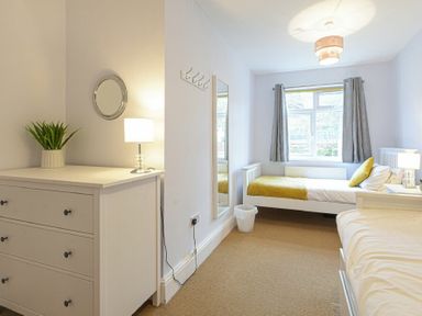 A bedroom with two single beds a chest of drawers with a lamp and plant a wall mirror and window with curtains at Bellshill Cottage in Belford