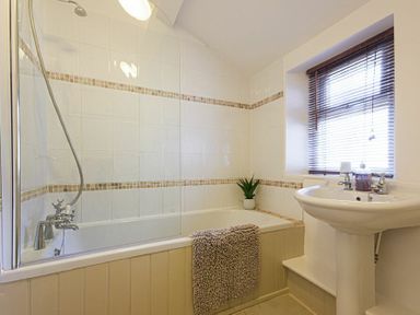 A bathroom with a bathtub shower combination a sink and a window with blinds at Bellshill Cottage in Belford