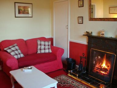 A living room with a red sofa a white coffee table and a fireplace at Briar Cottage in Town Yetholm and Kirk Yetholm