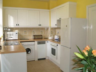 A kitchen with white cabinets appliances countertop and a bouquet of flowers at Briar Cottage in Town Yetholm and Kirk Yetholm