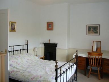 A bedroom with a black metal bed frame, floral bedspread, wooden desk with mirror, chair, and small fireplace at Briar Cottage in Town Yetholm and Kirk Yetholm