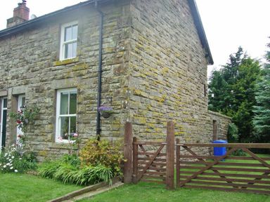 Stone house with white framed windows garden plants and wooden gate at Briar Cottage in Town Yetholm and Kirk Yetholm
