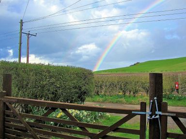 A wooden gate opening to a road with hedges green fields and a rainbow in the sky at Briar Cottage in Town Yetholm and Kirk Yetholm
