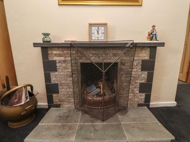 A fireplace with a metal fireguard and firewood a clock and sculptures on the mantel at Budle Bay Cottage in Bamburgh