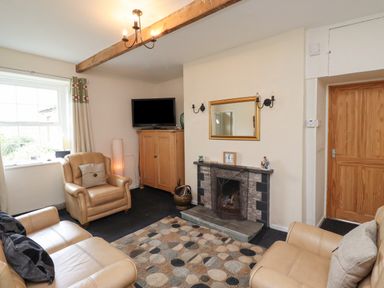 A living room with beige leather sofas a fireplace a wooden cabinet a television and a patterned rug at Budle Bay Cottage in Bamburgh