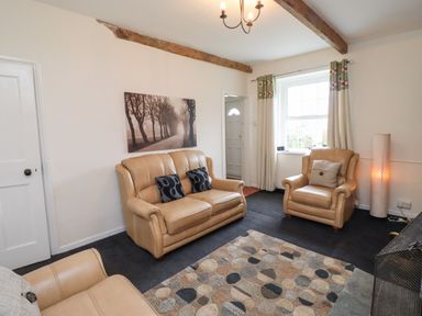 A living room with beige leather sofas a patterned rug and a window with curtains at Budle Bay Cottage in Bamburgh