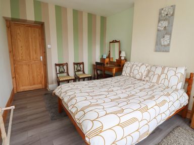 A bedroom with a bed two chairs a dressing table and a door at Budle Bay Cottage in Bamburgh