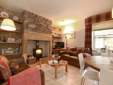 A living room with leather sofas a fireplace wooden shelves and a dining table at Coquet Cottage Warkworth