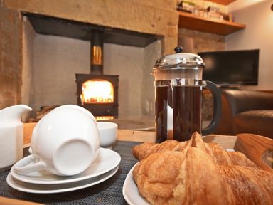 A tray with a French press, croissants, and cups in front of a wood stove fire in a living room at Coquet Cottage Warkworth