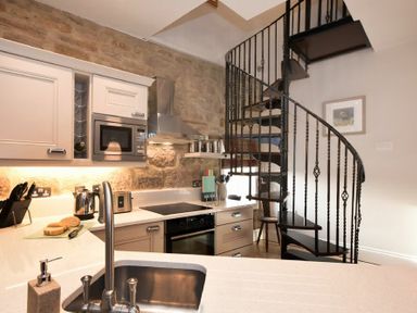 A kitchen with a sink a microwave a kettle and a spiral staircase at Coquet Cottage Warkworth