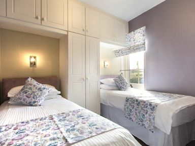 A bedroom with two single beds with floral bedding and built-in white cupboards at Coquet Cottage Warkworth