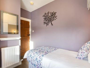 A bedroom with a single bed with floral bedding a wooden door a wall-mounted mirror and a metal wall decoration at Coquet Cottage Warkworth
