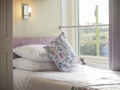 A bed with two white pillows and a floral cushion next to a window with a curtain at Coquet Cottage Warkworth