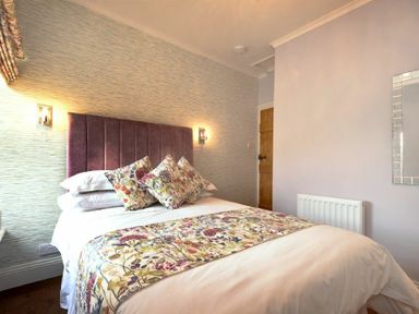 A bedroom with a bed featuring floral cushions and a matching runner at Coquet Cottage Warkworth