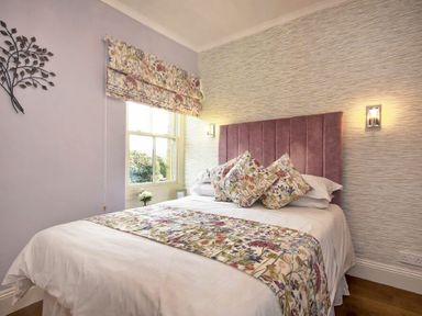 A bedroom with a bed that has floral pillows and runner with a floral window shade at Coquet Cottage Warkworth