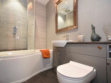 A bathroom with a toilet a sink a bathtub with a shower and an orange towel at Coquet Cottage Warkworth