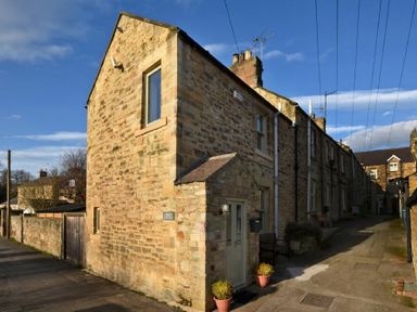 A stone cottage on a narrow street with potted plants at Coquet Cottage Warkworth