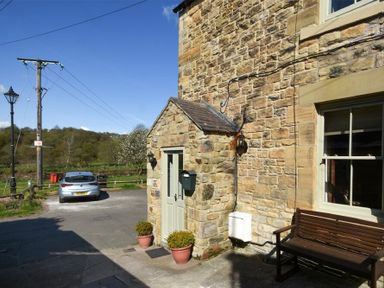 Stone house exterior with a door flanked by two potted plants a wooden bench and a parked car at Coquet Cottage Warkworth