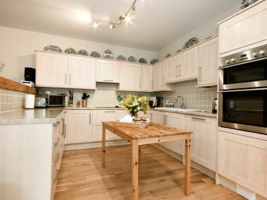A kitchen with wooden cabinets a wooden table with flowers and kitchen appliances at Craster Tower Coach House in Craster