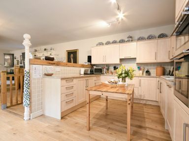 A kitchen with wooden cabinets a wooden table with flowers on it and various kitchen appliances at Craster Tower Coach House in Craster
