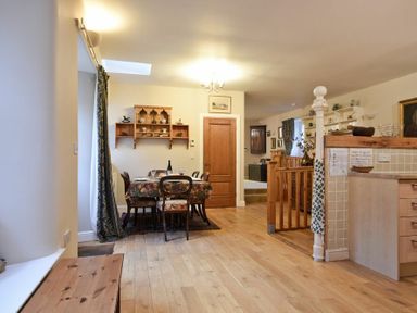 A dining area with a table and chairs next to a wooden door and an open kitchen at Craster Tower Coach House in Craster