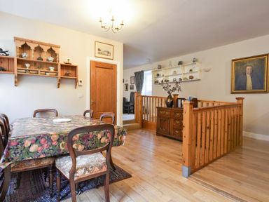 A dining area with a table covered by a floral tablecloth and wooden chairs wooden shelving and a wooden staircase railing in a room at Craster Tower Coach House in Craster