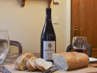 A table with sliced bread a knife a bottle of red wine and a glass with wine in a dining room at Craster Tower Coach House in Craster