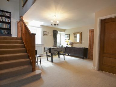 A room with carpeted stairs a foosball table a wooden cabinet and a bookshelf at Craster Tower Coach House in Craster