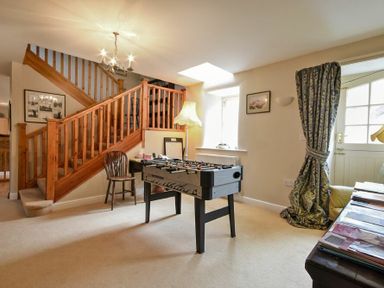 A room with a foosball table wooden stairs a chair a floor lamp and a window with curtains at Craster Tower Coach House in Craster