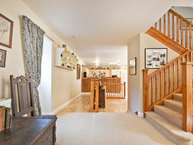 A hallway with wooden stairs and a wooden chair near a curtained window at Craster Tower Coach House in Craster