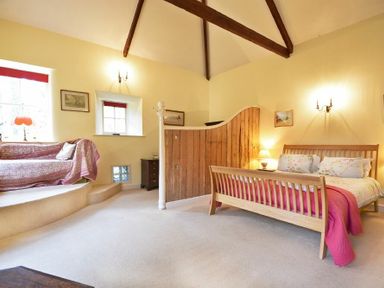 A bedroom with a wooden bed, a wooden partition, a raised seating area with a couch, and exposed ceiling beams at Craster Tower Coach House in Craster
