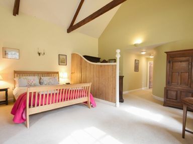 A bedroom with a wooden bed and a pink bedspread at Craster Tower Coach House in Craster