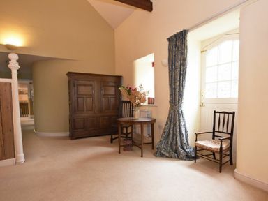 A room with two wooden chairs a small round table with flowers a wooden cabinet and a door with a blue patterned curtain at Craster Tower Coach House in Craster