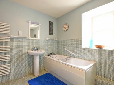 A bathroom with a bathtub sink mirror and window at Craster Tower Coach House in Craster