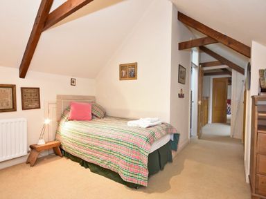 A bedroom with a single bed plaid bedding and wooden beams on the ceiling at Craster Tower Coach House in Craster