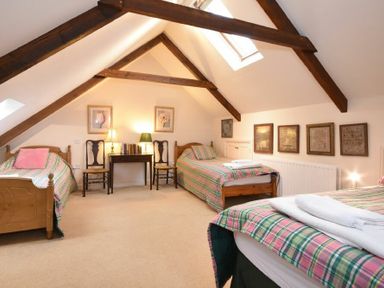 A bedroom with three single beds under a sloped ceiling with exposed wooden beams at Craster Tower Coach House in Craster