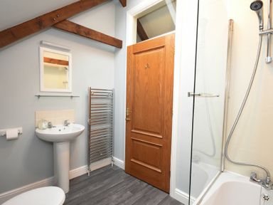 A bathroom with a sink mirror towel rail wooden door and a shower over a bathtub at Craster Tower Coach House in Craster