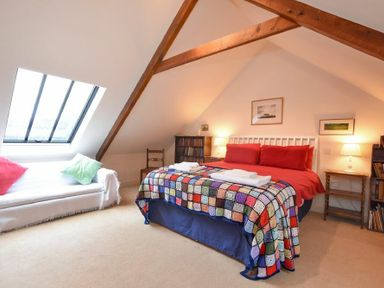 A bedroom with a bed covered in a colorful blanket next to a sofa with cushions under a skylight at Craster Tower Coach House in Craster