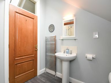 A bathroom with a wooden door a white pedestal sink a wall mirror towel rack and toilet paper holder at Craster Tower Coach House in Craster