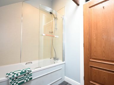 A bathroom with a bathtub shower combination glass shower screen and a wooden door with a towel on the tub at Craster Tower Coach House in Craster